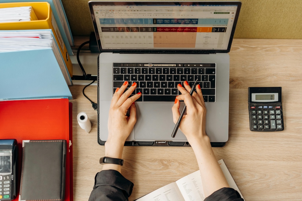 photo prise du dessus d'un bureau avec un ordinateur portable et des mains de femme vernis posés sur le clavier